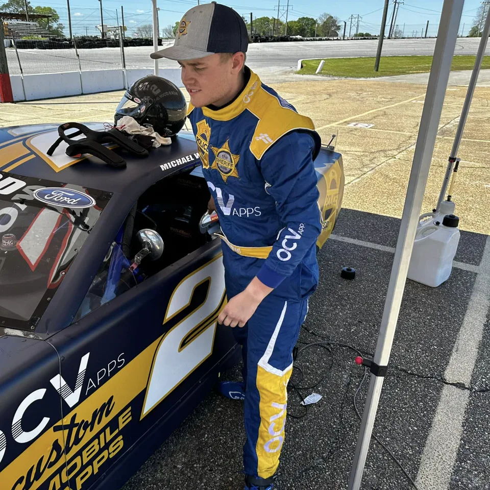 Mike Wood in his blue and yellow FervoGear suit beside his number 2 race car Mike Wood in his blue and yellow FervoGear suit beside his number 2 race car
